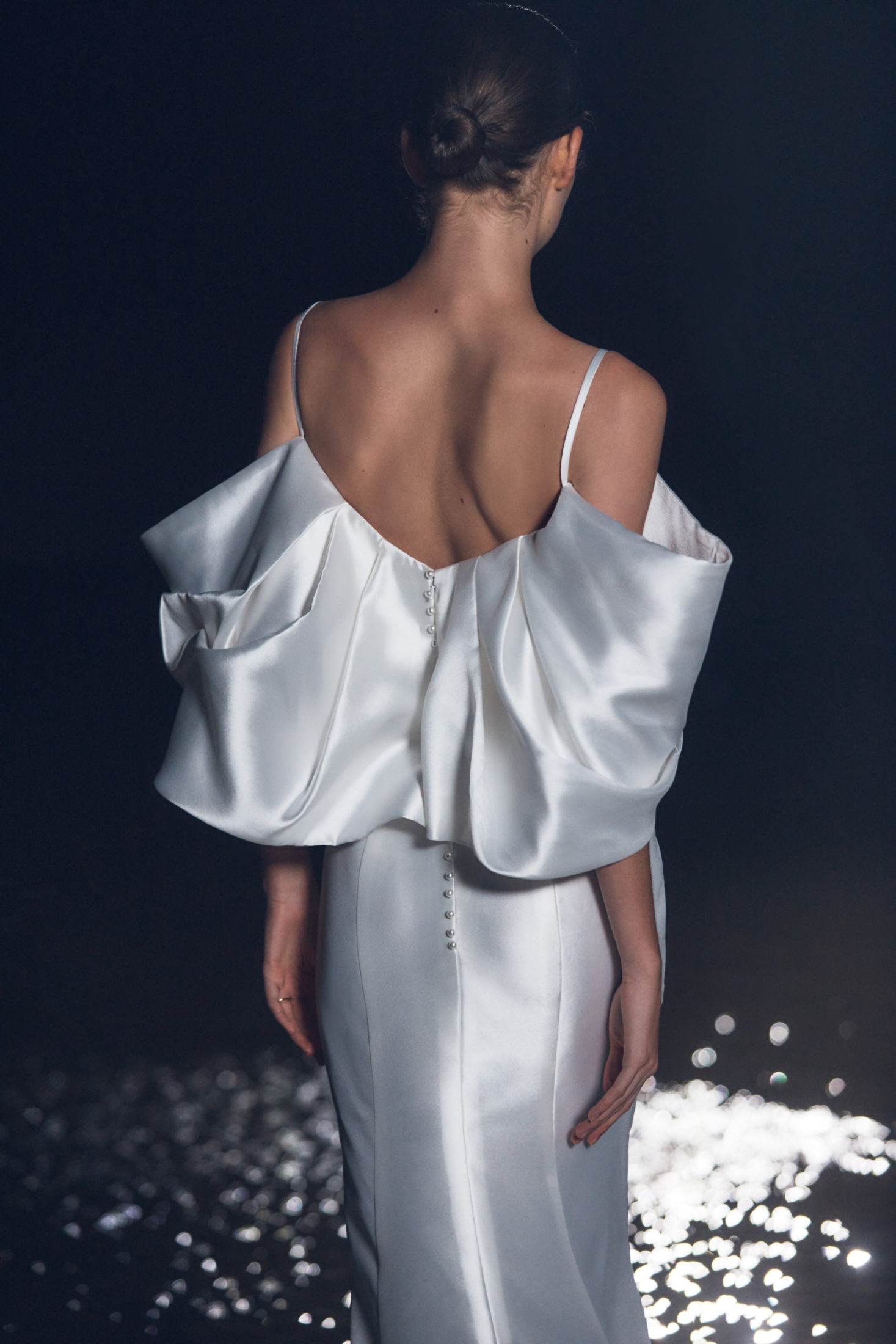 Back shot of a Hera Couture Wedding Gown with off the shoulder, exaggerated sleeves. Lustrous fabrication that glints under the moonlight on the runway.